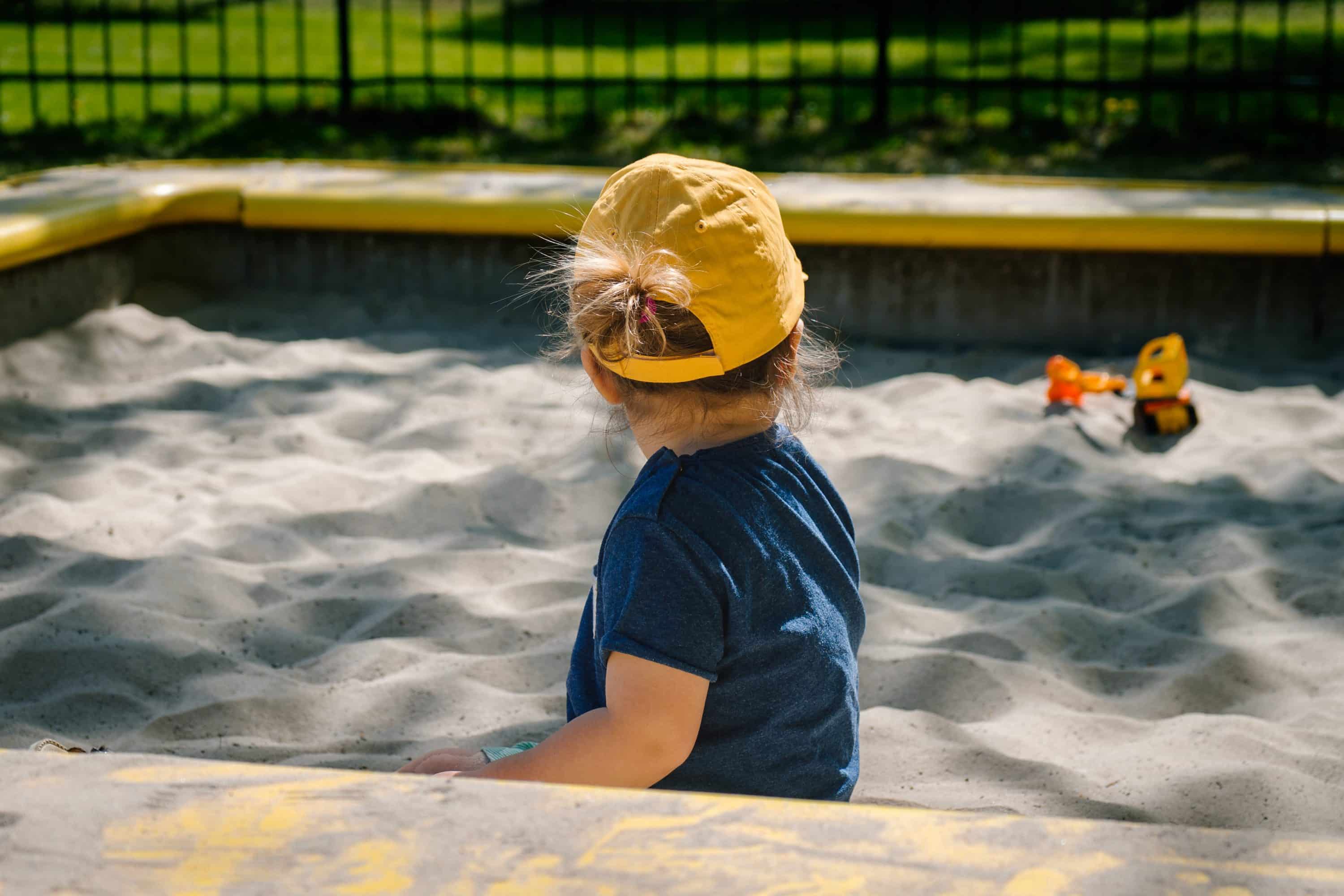 school sandpit with child playing wearing a yellow hat
