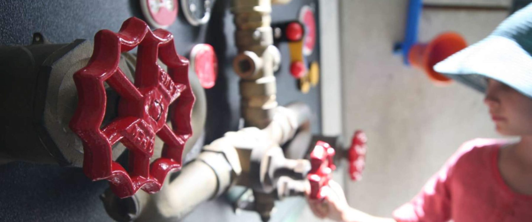 A child turning a red gear on a wall